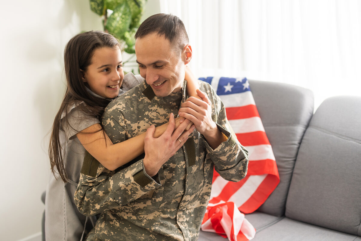 A Child Girl Hugs A Military Father. Dad In Military Uniform Wit
